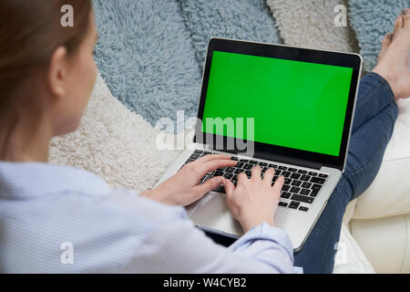 Over The Shoulder View Of Woman Lying On Sofa Using Green Screen Laptop Stock Photo