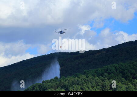 Firefighting helicopter intervenes for the fire that starts on the forest-covered mountain. Stock Photo
