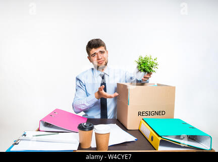 The young man is resigned and folds things in the workplace, folders, documents. Couldn't cope with responsibilities. Concept of office worker's troubles, business, advertising, resignation problems. Stock Photo