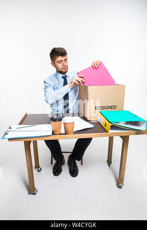 The young man is resigned and folds things in the workplace, folders, documents. Couldn't cope with responsibilities. Concept of office worker's troubles, business, advertising, resignation problems. Stock Photo