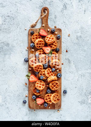 Small round delicious soft belgian waffles on cutting board. Fresh belgian waffles with berries and caramel sauce top view. Copy space for text or mock up. Vertical Stock Photo