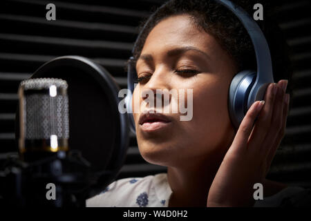 Female Vocalist Wearing Headphones Singing Into Microphone In Recording Studio Stock Photo