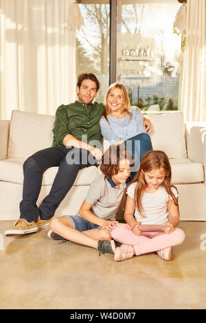 Siblings play with the tablet Computer and parents are watching on the sofa Stock Photo
