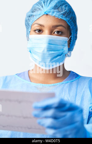 Studio Portrait Of Female Surgeon Wearing Gown And Mask Holding Medical Print Out Stock Photo