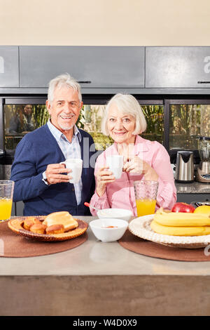 Happy pensioner couple with mug of coffee having breakfast in the morning in the kitchen Stock Photo