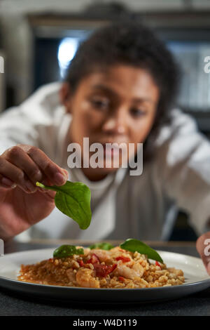 Female Chef Garnishing Plate Of Food In Professional Kitchen Stock Photo