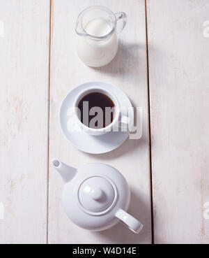 Cup of coffee, teapot and jug with milk in row over white wooden background. Flat lay, copy space. Stock Photo