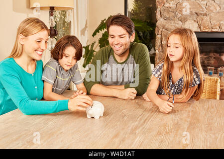 Smiling mother puts money in a piggy bank and her children and father watch Stock Photo