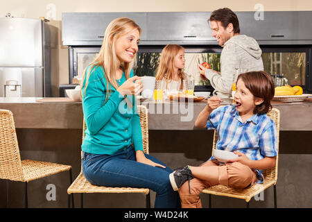 Mother and son have breakfast in the kitchen with father and sister in the background Stock Photo