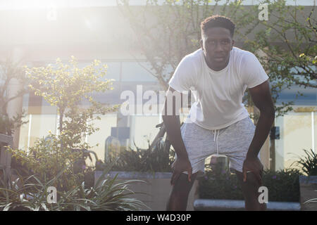 Portrait of African American man taking a rest during jogging. Young male fit person doing exercise and taking a break in city park Stock Photo