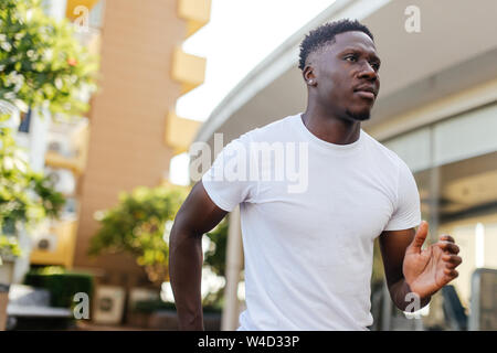African American man jogging in the city park. Young male fit person in white shirt running outdoors Stock Photo