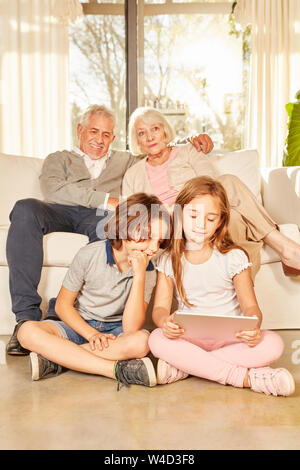 Grandchildren are surfing the internet using the tablet PC and grandparents are watching on the sofa Stock Photo