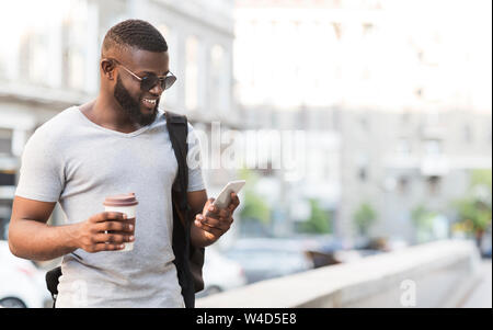 Cheerful african man using his smartphone and drinking coffee Stock Photo