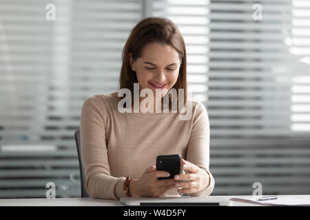 Smiling businesswoman using smartphone looking at phone at workplace Stock Photo