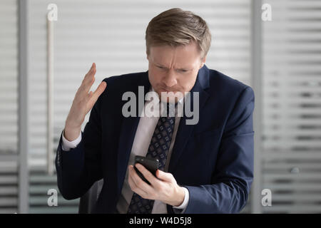 Angry stressed business man wear suit frustrated with phone problem Stock Photo