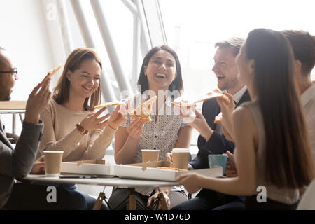 Cheerful multicultural team workers laugh share lunch meal eating pizza Stock Photo