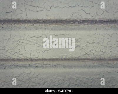 Grey paint peeling off a metallic surface background. Old grungy, weathered painted wall texture. Cracked, dirty, silver plaster falling off the const Stock Photo