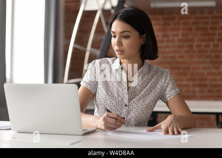Focused asian business woman working looking at laptop making notes Stock Photo