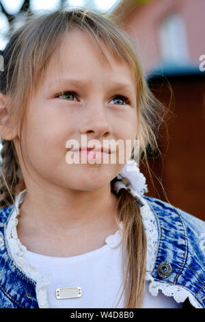 A girl with a pigtail in a denim jacket and white dress walks at sunset in the park. Vertical photo Stock Photo