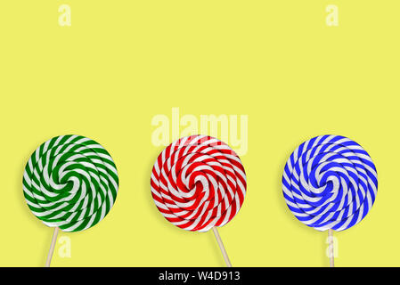 Sweet lollipops. Round large caramel candy. Three multi-colored candy on a yellow background. Green, Blue and Red Stock Photo