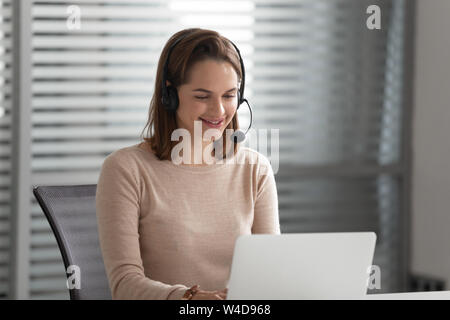 Smiling businesswoman receptionist wear wireless headset video calling on computer Stock Photo