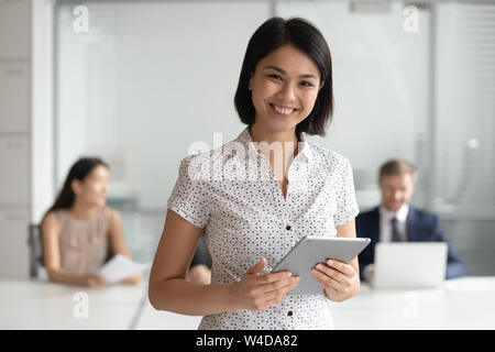 Happy female asian manager looking at camera holding digital tablet Stock Photo