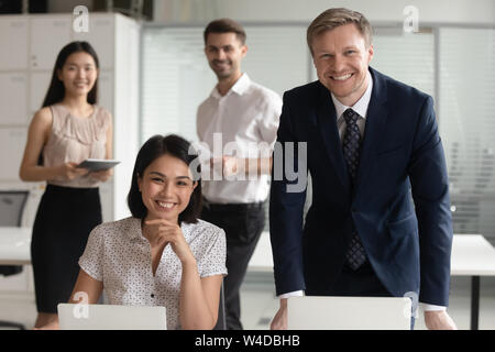 Smiling diverse business leaders posing with computers and team people Stock Photo