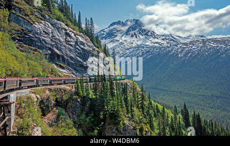 Skagway, Alaska, USA - May 22, 2019 The White Pass & Yukon Route Railroad travels along the rails below Slippery Rock on the way to Skagway. Stock Photo