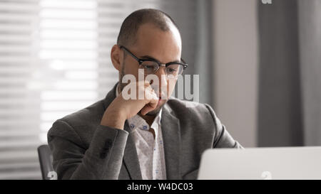 Focused african businessman thinking solving business problem looking at laptop Stock Photo