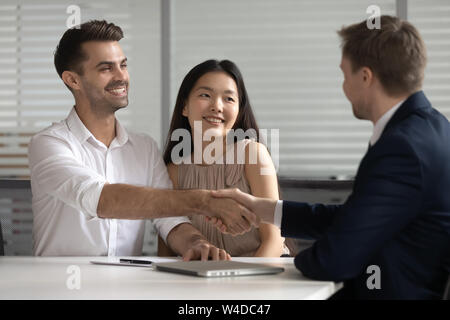 Smiling mixed ethnicity young spouses couple customers handshake bank manager Stock Photo