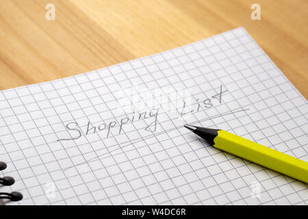 Yellow pencil on a notebook with sheets in a cage on a wooden table. Sign Shopping List. Stock Photo