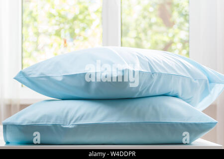 Closeup of two blue pillows lie on a dresser against the background of a blurred window. Household. Stock Photo