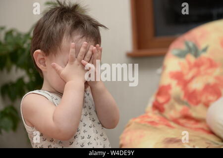 Boy playing hide-and-seek game at home. Portrait of boy male clothing eyes with hands Stock Photo