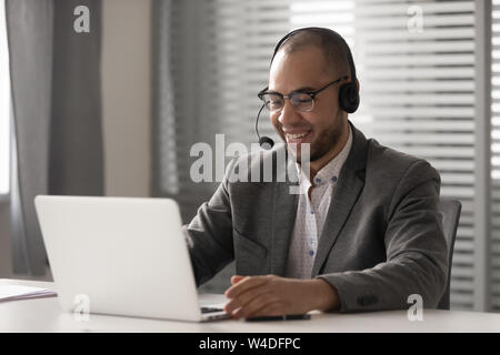 Smiling african man wearing wireless headset video calling on computer Stock Photo