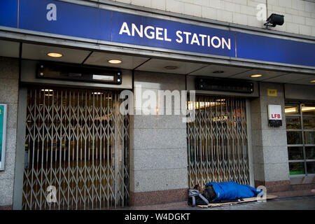 London. Islington. Angel Station. Homeless man sleeping on the pavement, next to locked underground entrance. Stock Photo