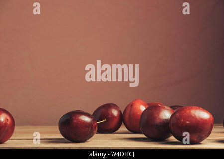 Fresh red plums on a brown table. Beautiful dark red wall background. Stock Photo