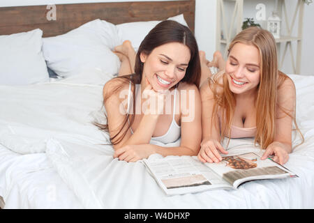 Friends together at home lying on bed reading magazine happy Stock Photo