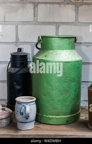 An old green tin can beside a rusted tin can on a shelf in front of white bricks wall in frontal view. Stock Photo