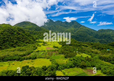 Aerial drone view of clouds passing over lush greenfarmland with mountains and volcanos in the background (Camiguin, Philippines) Stock Photo