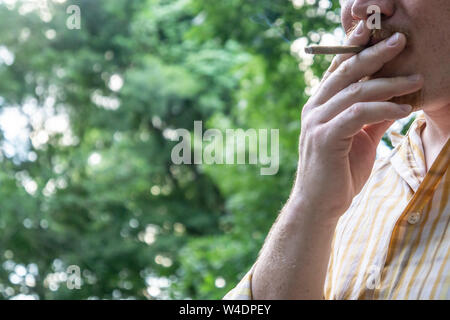 Male working man wearing button down collared shirt holding and smoking marijuana blunt joint for relaxation with blank empty room space for copy or t Stock Photo