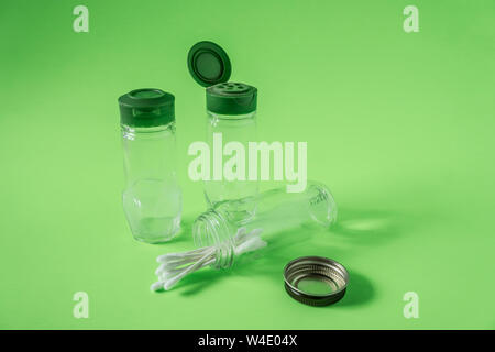 3 Glass spice jars on lime green background with blank empty room space for text or copy. Three kitchen bottles recycled and reused to store cotton sw Stock Photo