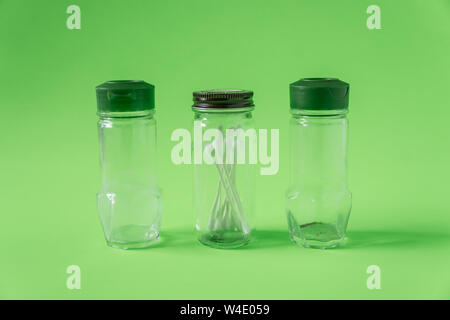 3 Glass spice jars on lime green background with blank empty room space for text or copy. Three kitchen bottles recycled and reused to store cotton sw Stock Photo