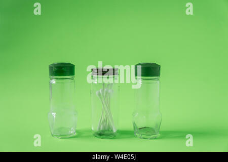 3 Glass spice jars on lime green background with blank empty room space for text or copy. Three kitchen bottles recycled and reused to store cotton sw Stock Photo