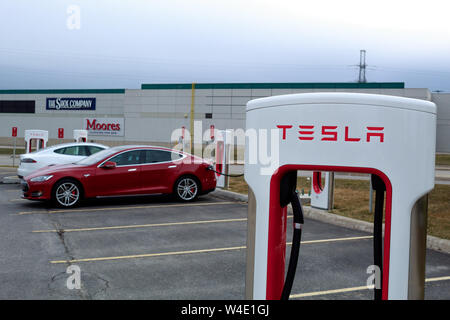 Tesla Supercharger in-front of two charging Tesla Model S's. Stock Photo