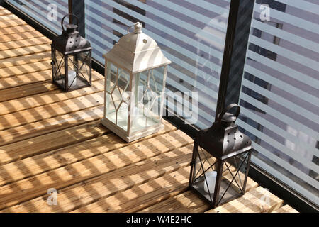 White and brown lanterns on a wooden floor during a sunny day. Photographed in balcony with striped glass fence making beautiful shadows. Closeup. Stock Photo