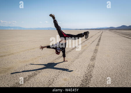 A young man does a cartwheel on the Black Rock Desert with tire tracks leading in the distance on a sunny day. Stock Photo