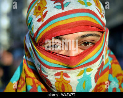 Young Indian woman covers her hair and face with a colourful and trendy secular headscarf. Stock Photo