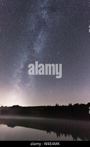 The Milky Way, surrounded by stars in the night sky, makes an appearence over a nearby reservoir during a cold winters night photography shoot. Stock Photo