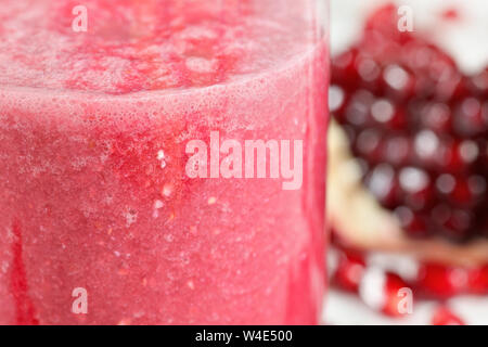 Pink pomegranate smoothie drink in glass, blurred halved fruit in background Stock Photo