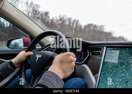Man behind the wheel of a Tesla Model S, as he drives down the highway. Stock Photo